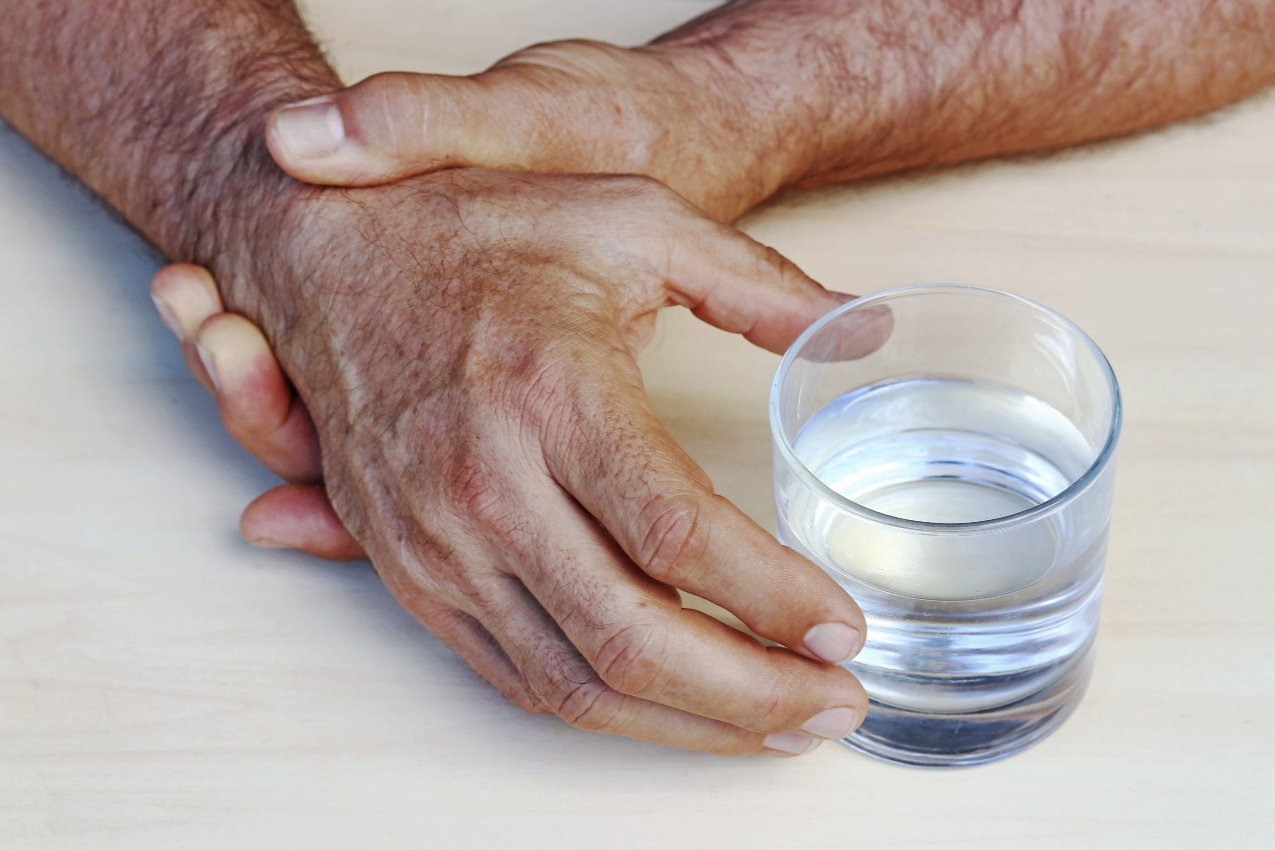 trembling hands of a Parkinson's patient finding it difficult to hold a glass of water.